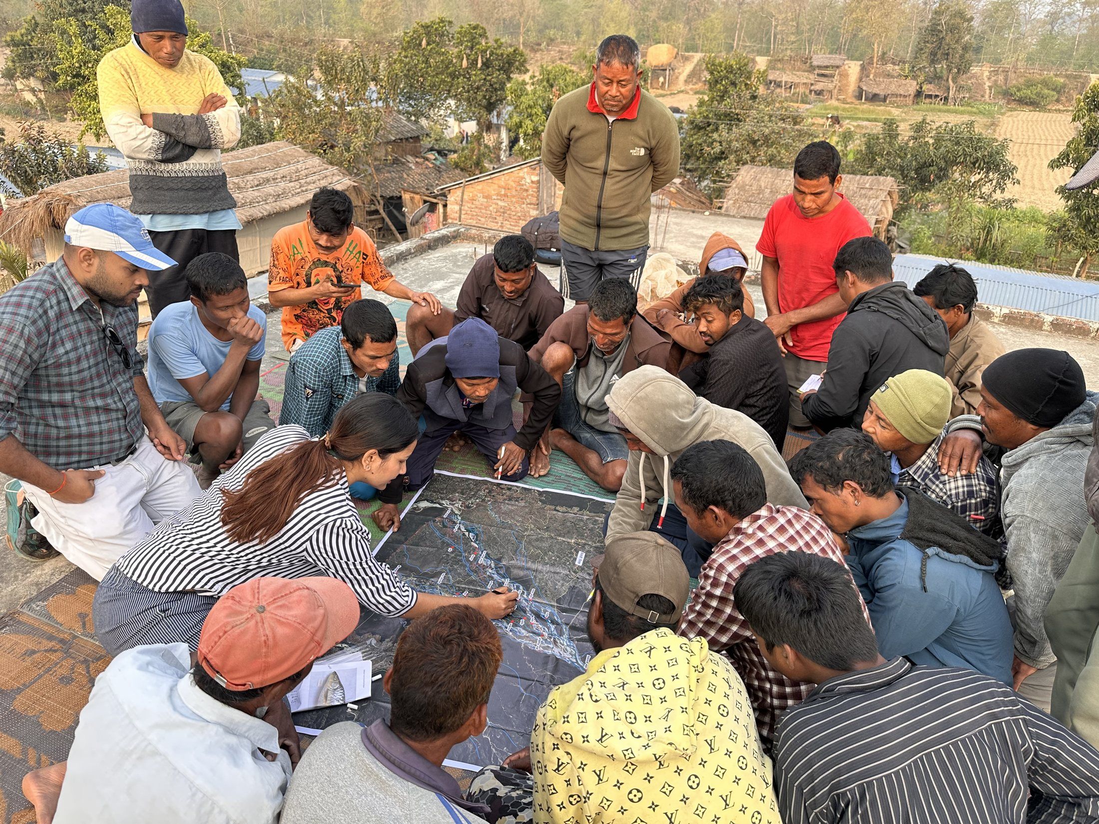 Elisha Ghimire leading a mapping session with community members gathered around a satellite map