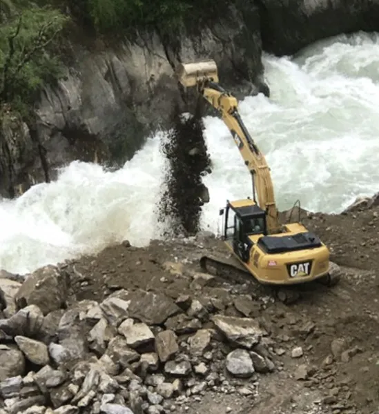 Excavator tipping rock and soil into a fast river